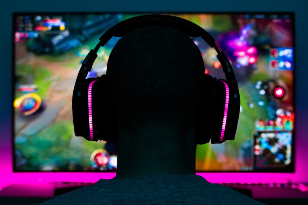 Stock photo of a gamer man with headphones playing a video game in front of the tv
